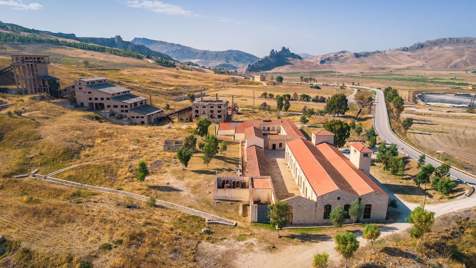 An abandoned industrial complex with multiple buildings and a winding road.