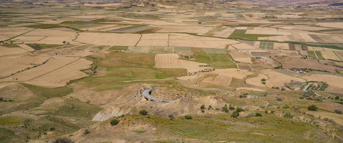 An aerial view of a rural landscape with fields, a winding road, and distant hills.