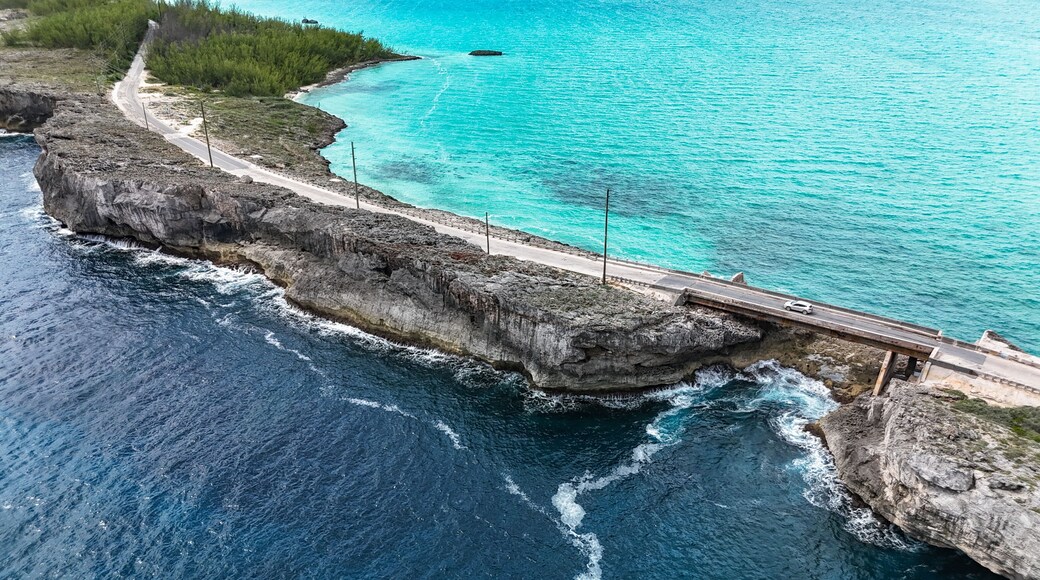 Aerial view of the Glass Window Bridge with a white car spanning a narrow rocky strip between the dark Atlantic Ocean and turquoise Caribbean waters in North Eleuthera, North Eleuthera, The Bahamas.