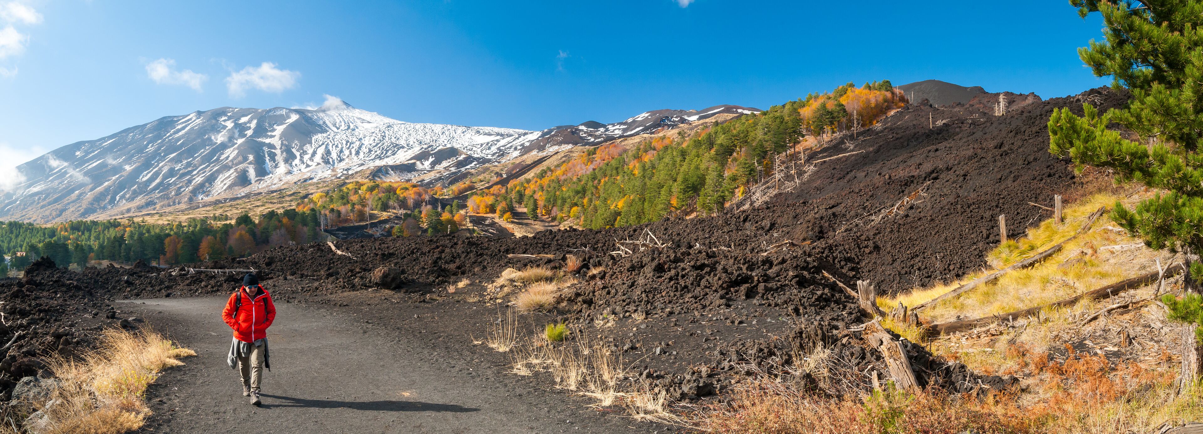 Mount Etna, Italy: panorama of the northern side of the volcano and a hiker walking on a lavic pathway