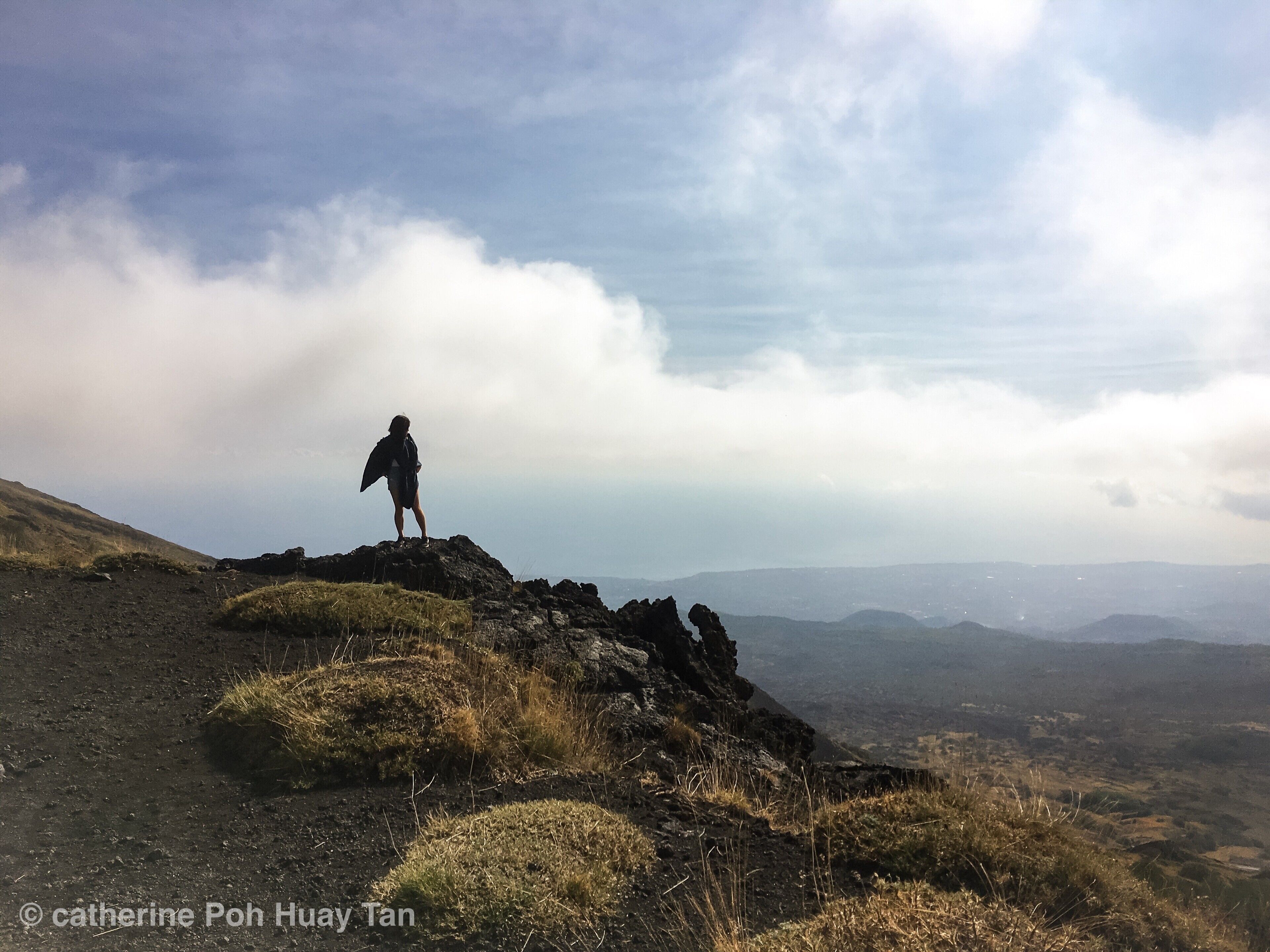 A person standing on a rocky hilltop with a vast landscape in the background.