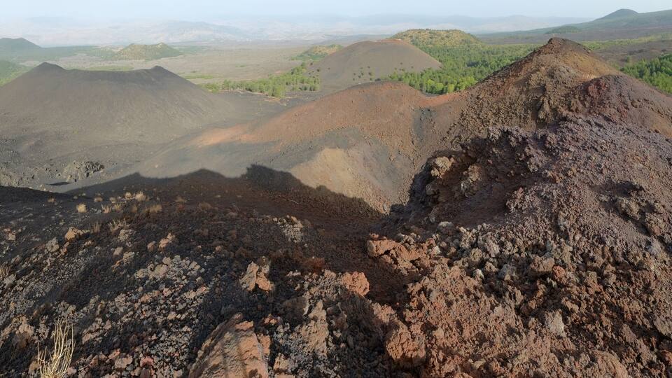 A volcanic landscape with rugged terrain and scattered vegetation.