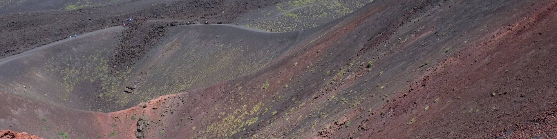A volcanic landscape with a prominent mountain, winding paths, and sparse vegetation.