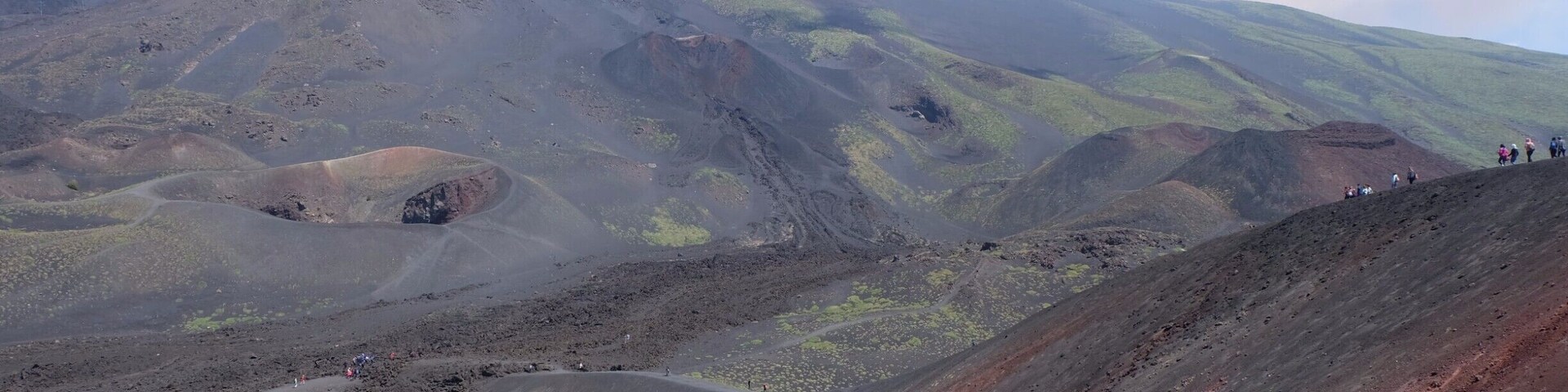 Un paisaje volcánico con una montaña destacada, senderos sinuosos y vegetación escasa.