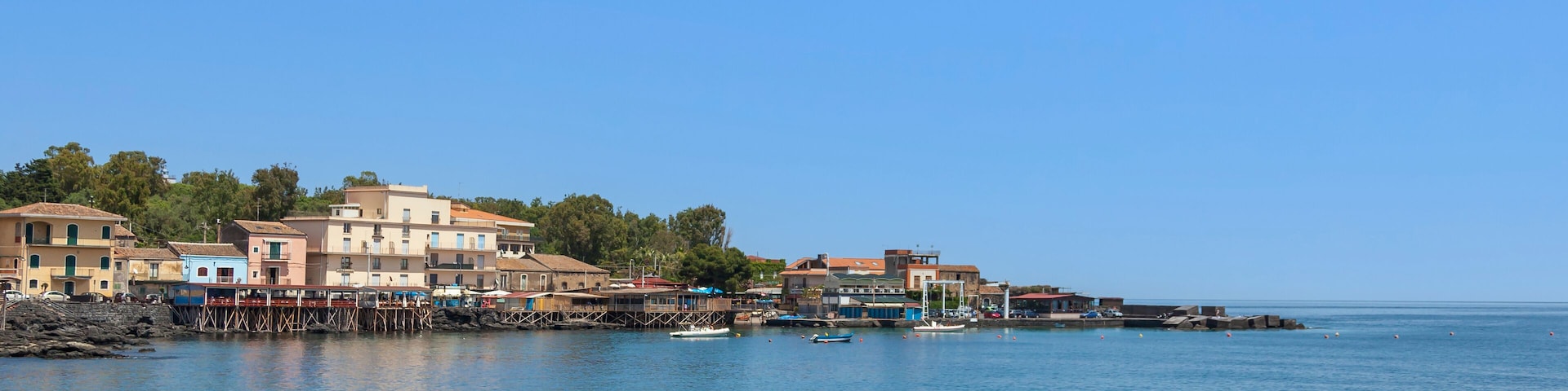 Un pueblo costero con edificios a lo largo del paseo marítimo, barcos y un cielo azul despejado.