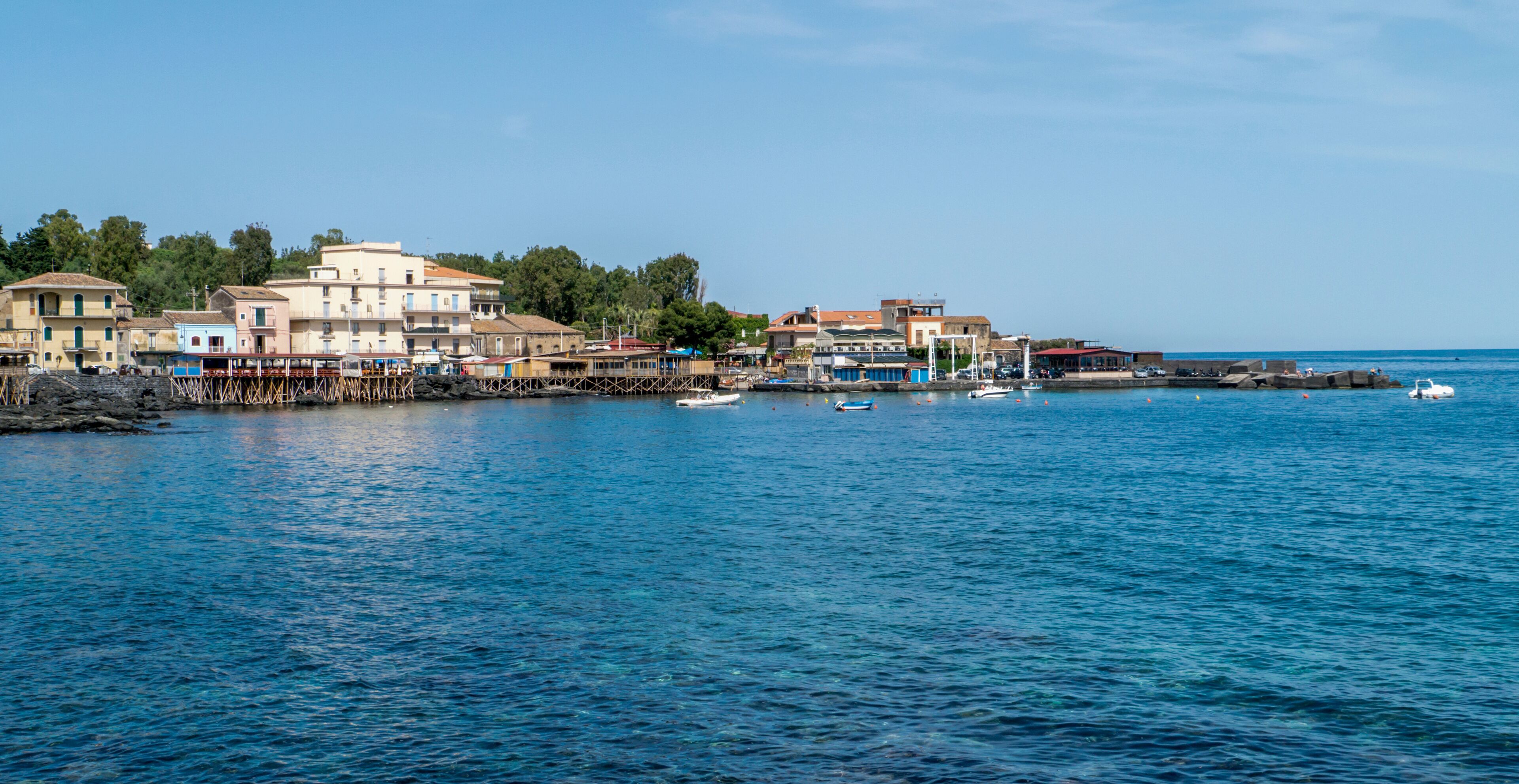 A coastal town with buildings along the waterfront, boats, and a clear blue sky.