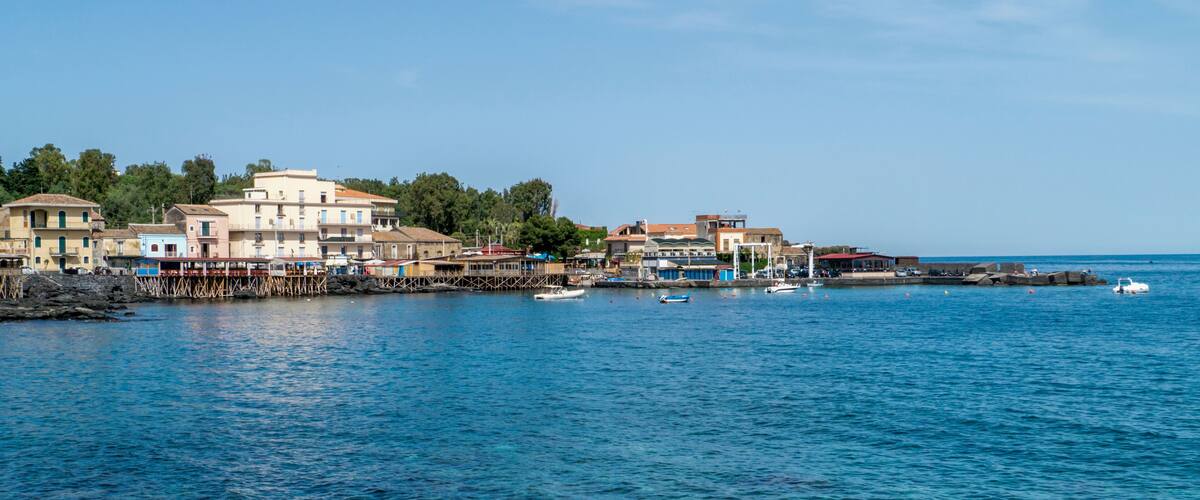 A coastal town with buildings along the waterfront, boats, and a clear blue sky.