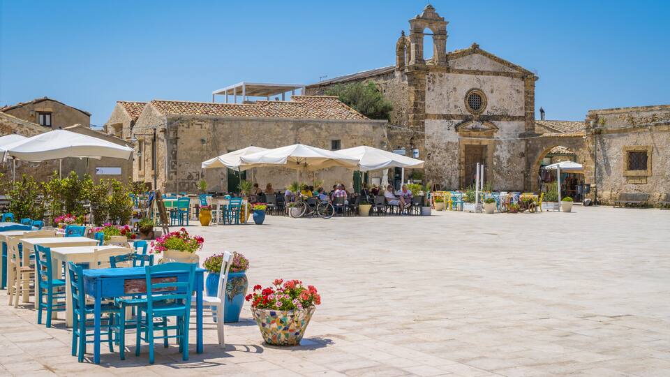 A plaza with outdoor seating, a historic church, and a clear blue sky.