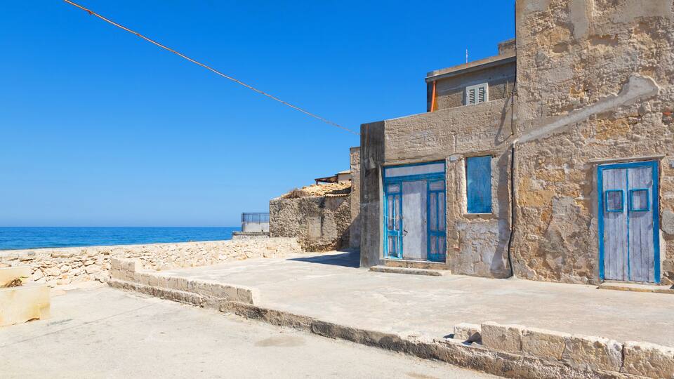 A coastal building with blue doors and windows, a clear blue sky, and the sea in the background.