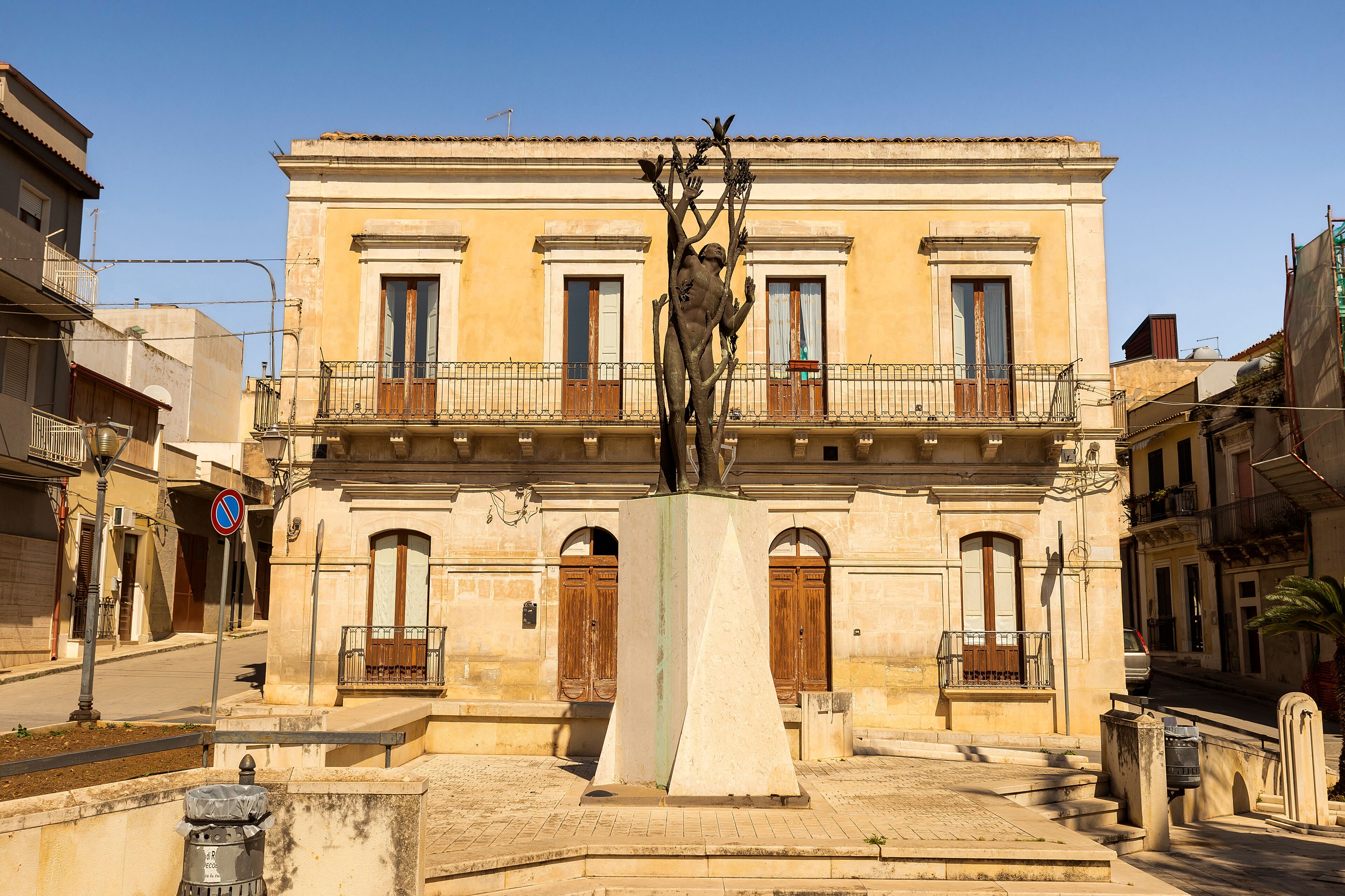 A statue in front of a yellow building with balconies and arched windows.