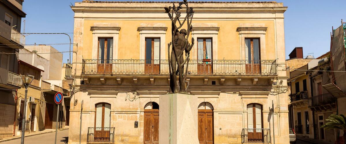 A statue in front of a yellow building with balconies and arched windows.