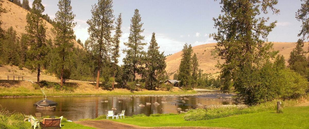 A river with a picnic area and chairs, surrounded by trees and hills.