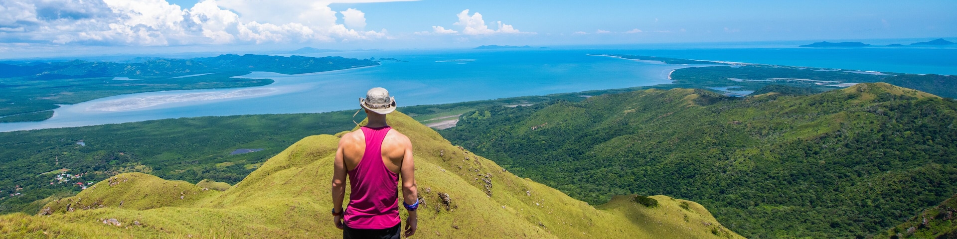 A person standing on a grassy hill overlooking a coastal landscape with a body of water and distant islands.