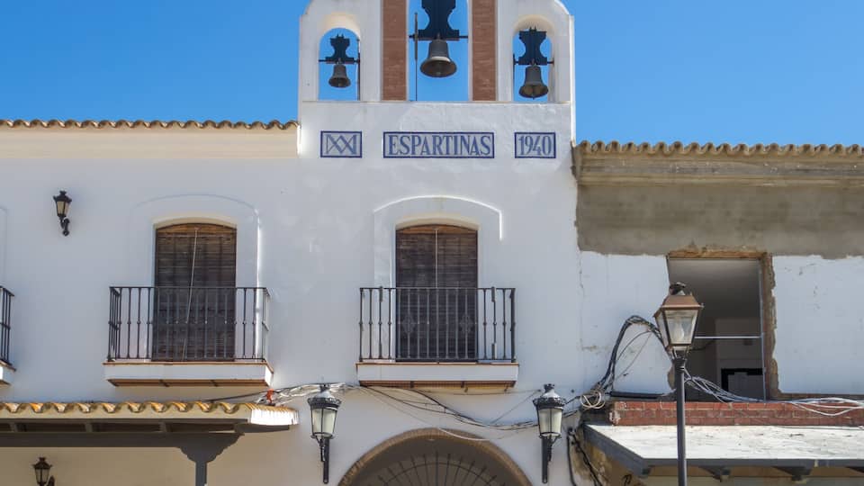 A white building with a bell tower, a wooden door, and a sign that reads "Espartinas 1940".