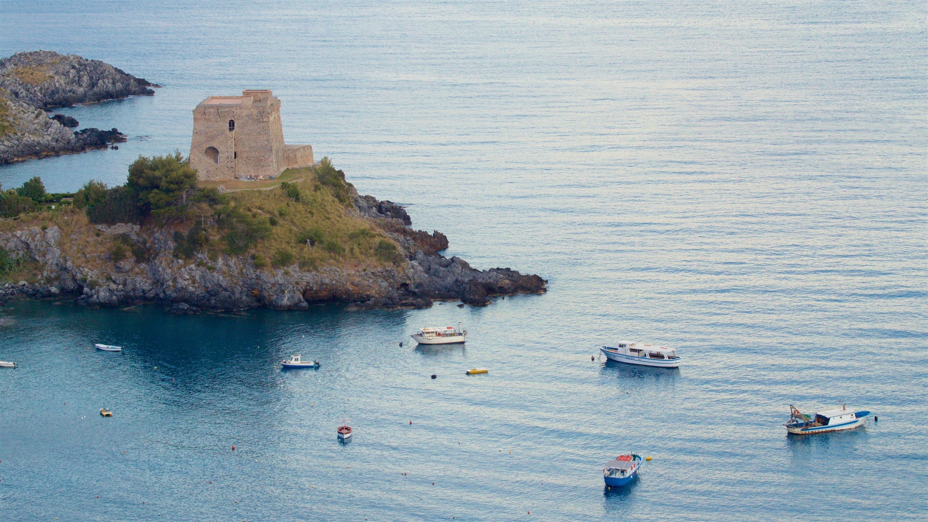 A coastal scene with a small island featuring a stone tower and several boats in the water.