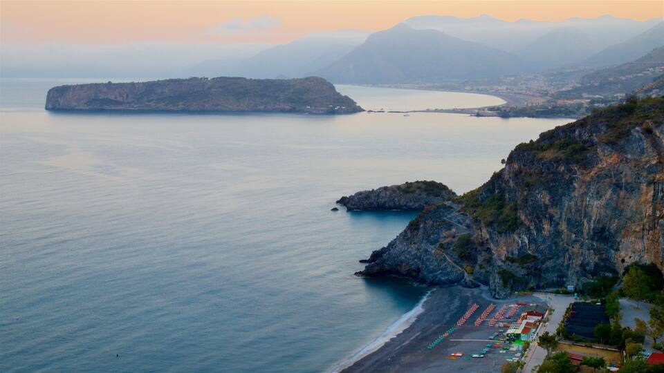 A coastal landscape with a beach, rocky cliffs, and a distant mountain range.