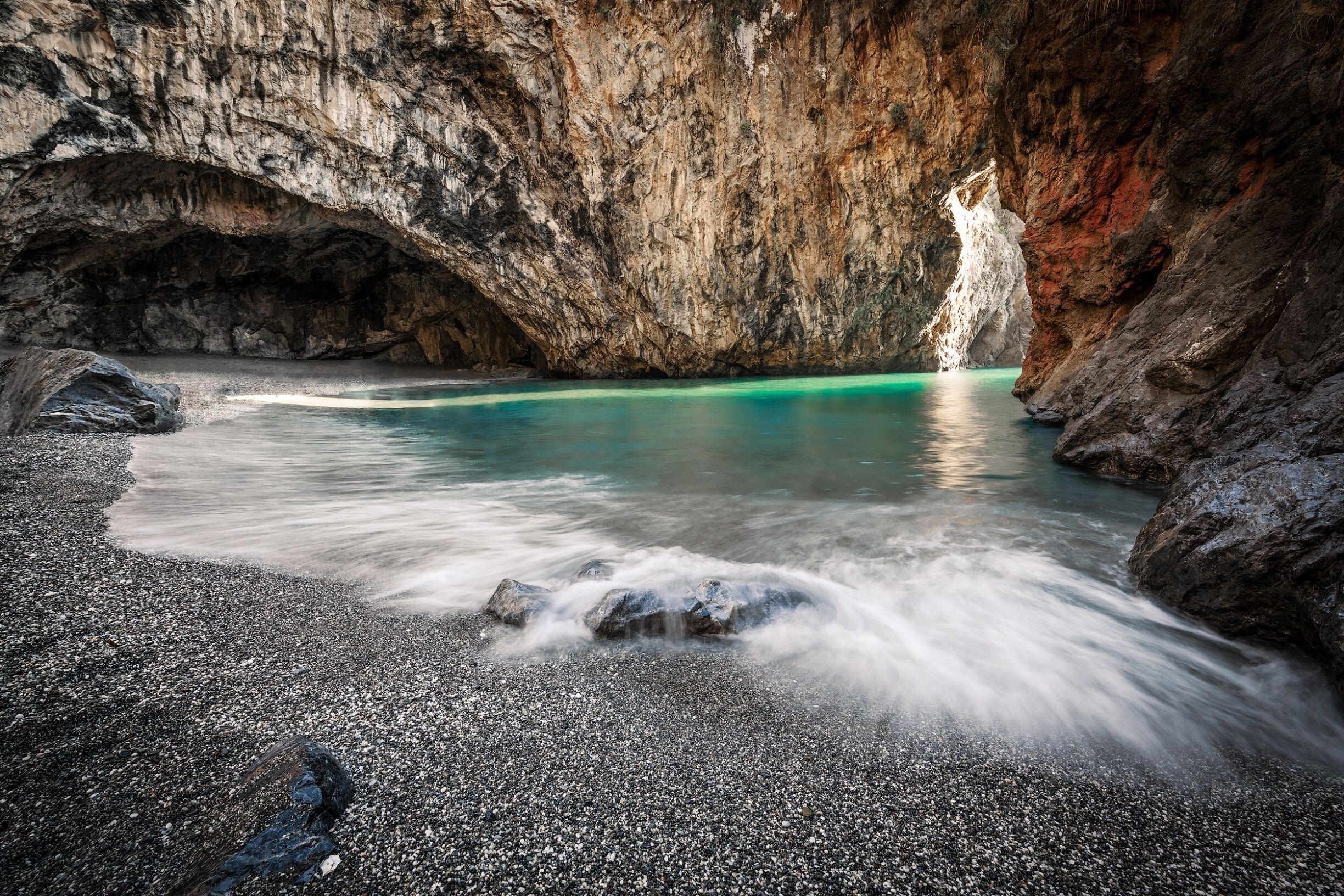 A rocky cave with turquoise water and a waterfall.