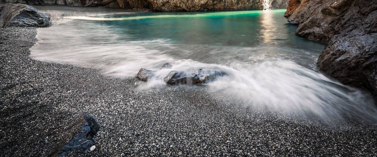 A rocky cave with turquoise water and a waterfall.