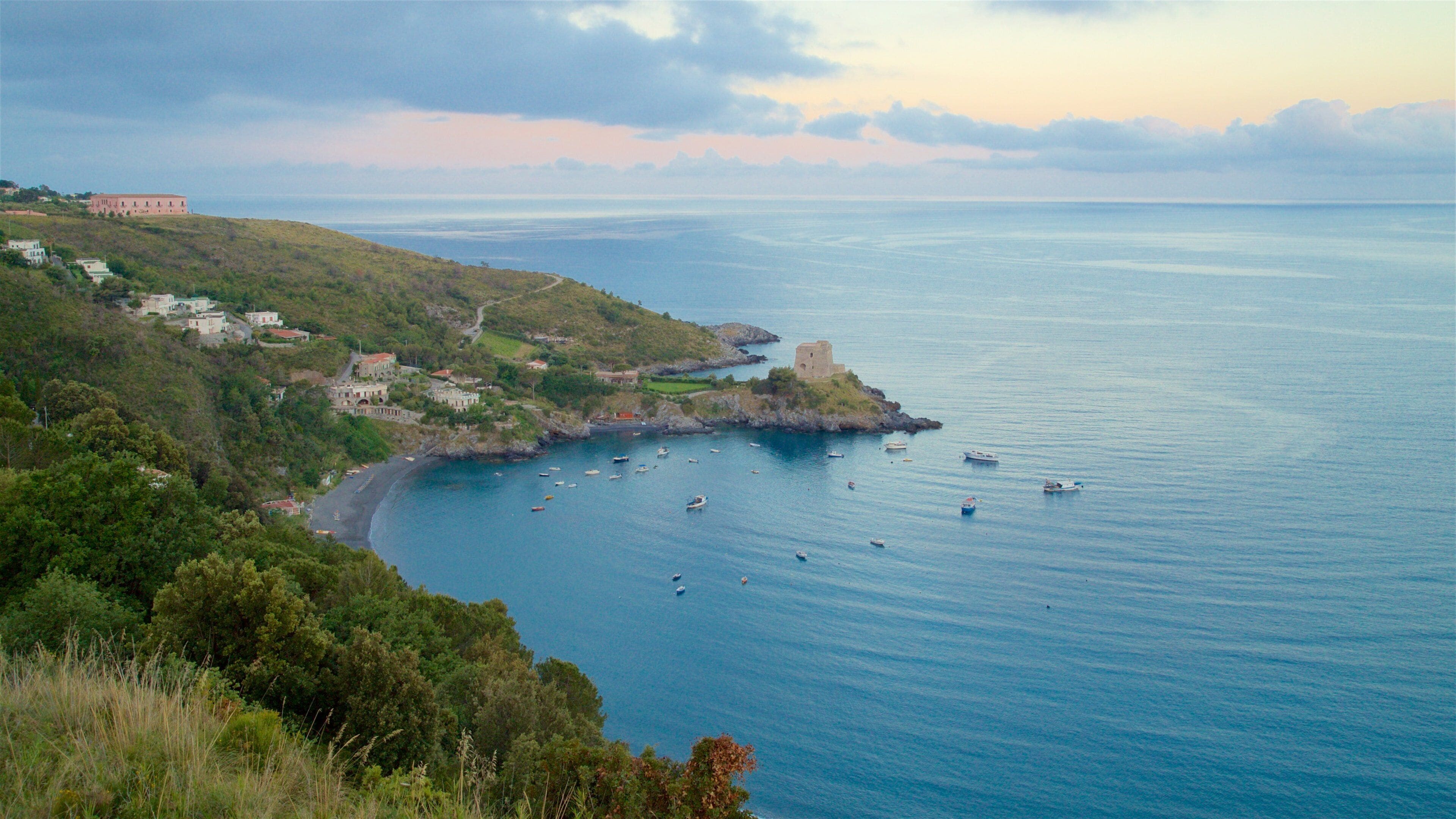 A coastal town with a castle, boats, and lush greenery.