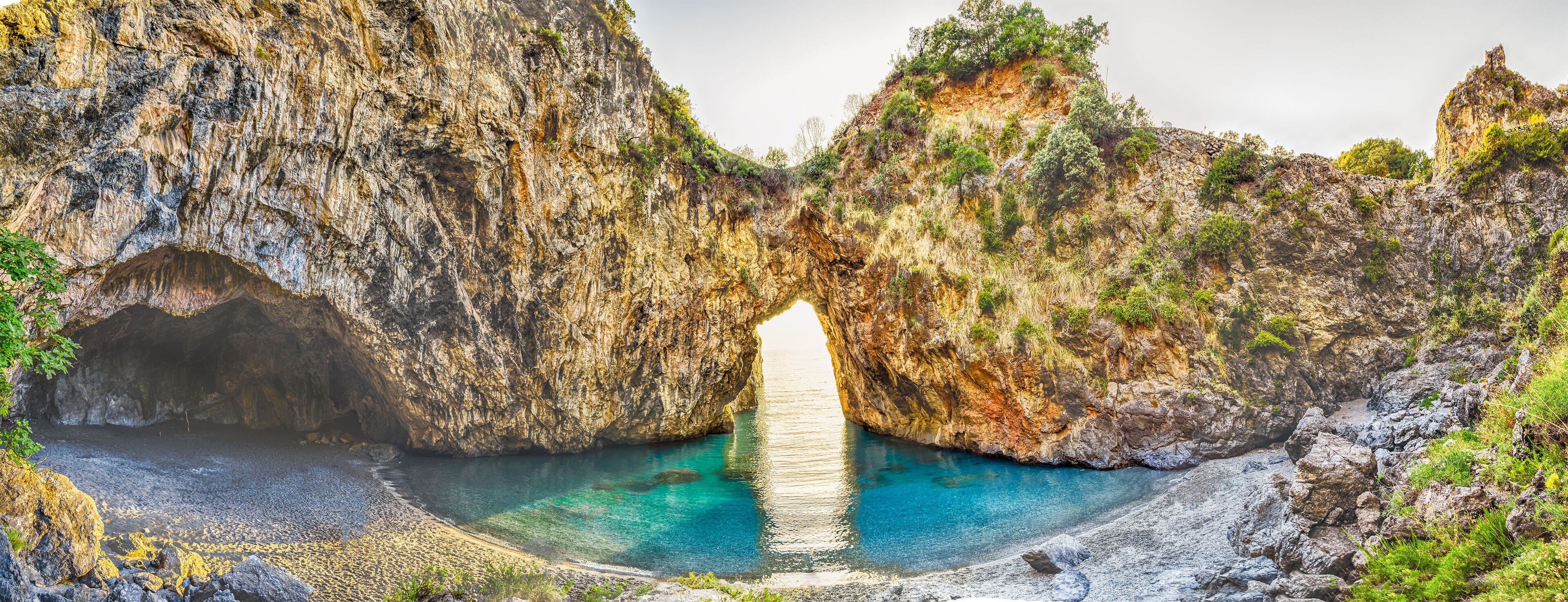 Paisaje costero con un arco natural de roca y un mar azul cristalino.