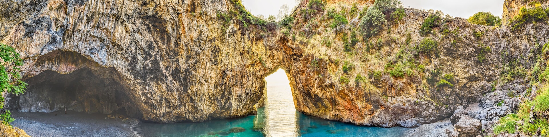 Paisaje costero con un arco natural de roca y un mar azul cristalino.