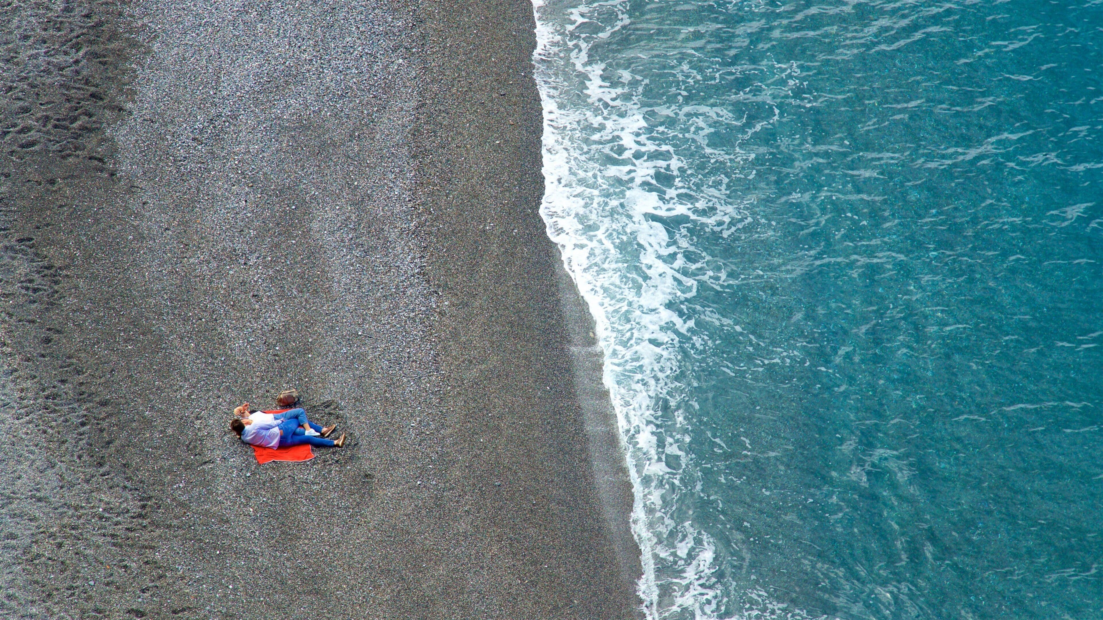 Vista aérea de uma praia com uma pessoa deitada em um tapete vermelho.