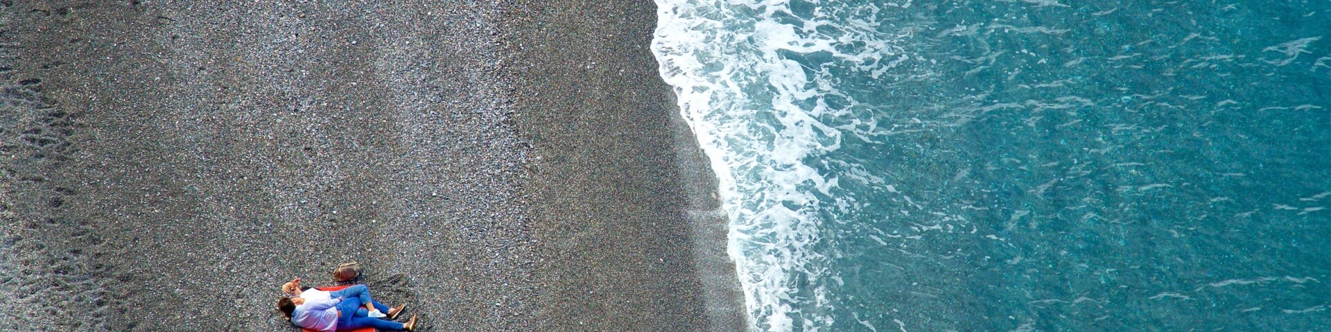 Vista aérea de uma praia com uma pessoa deitada em um tapete vermelho.
