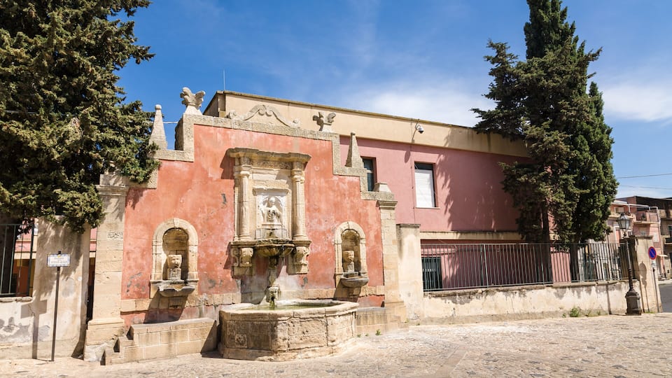 A historic building with a fountain, arched windows, and a statue.