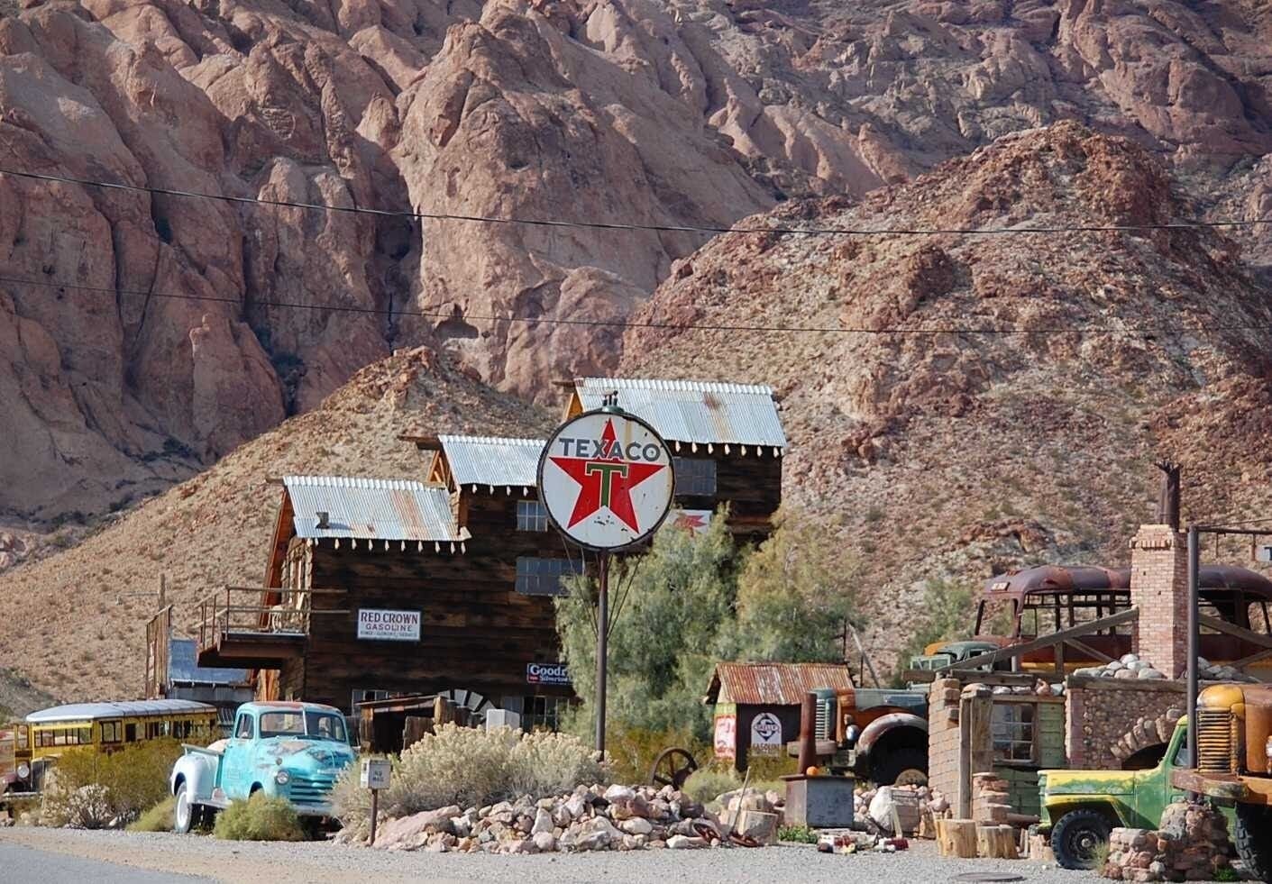A vintage Texaco gas station with a red star logo, surrounded by old vehicles and a mountainous backdrop.