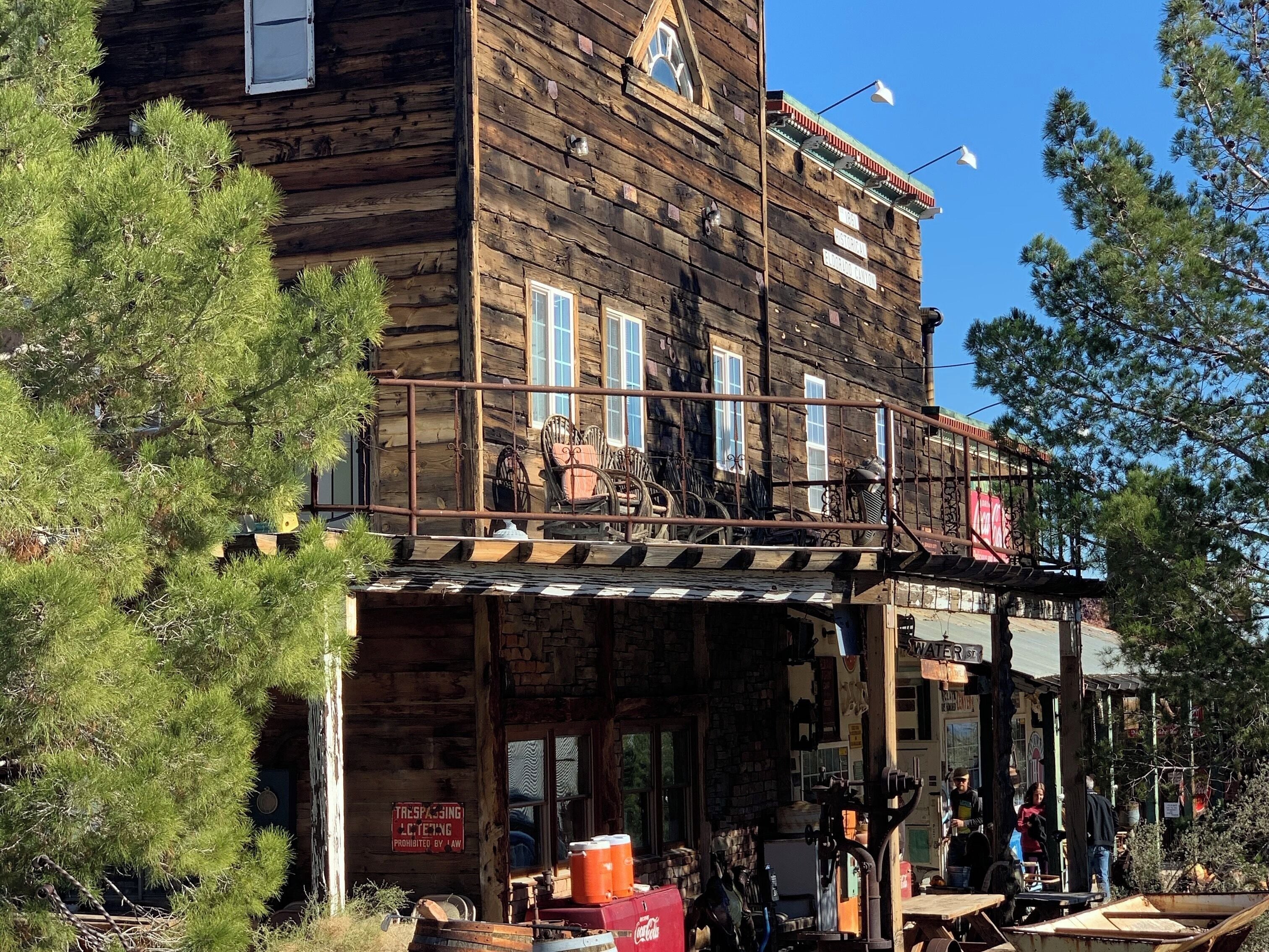 A rustic wooden building with a porch, vintage chairs, and a Coca-Cola cooler.