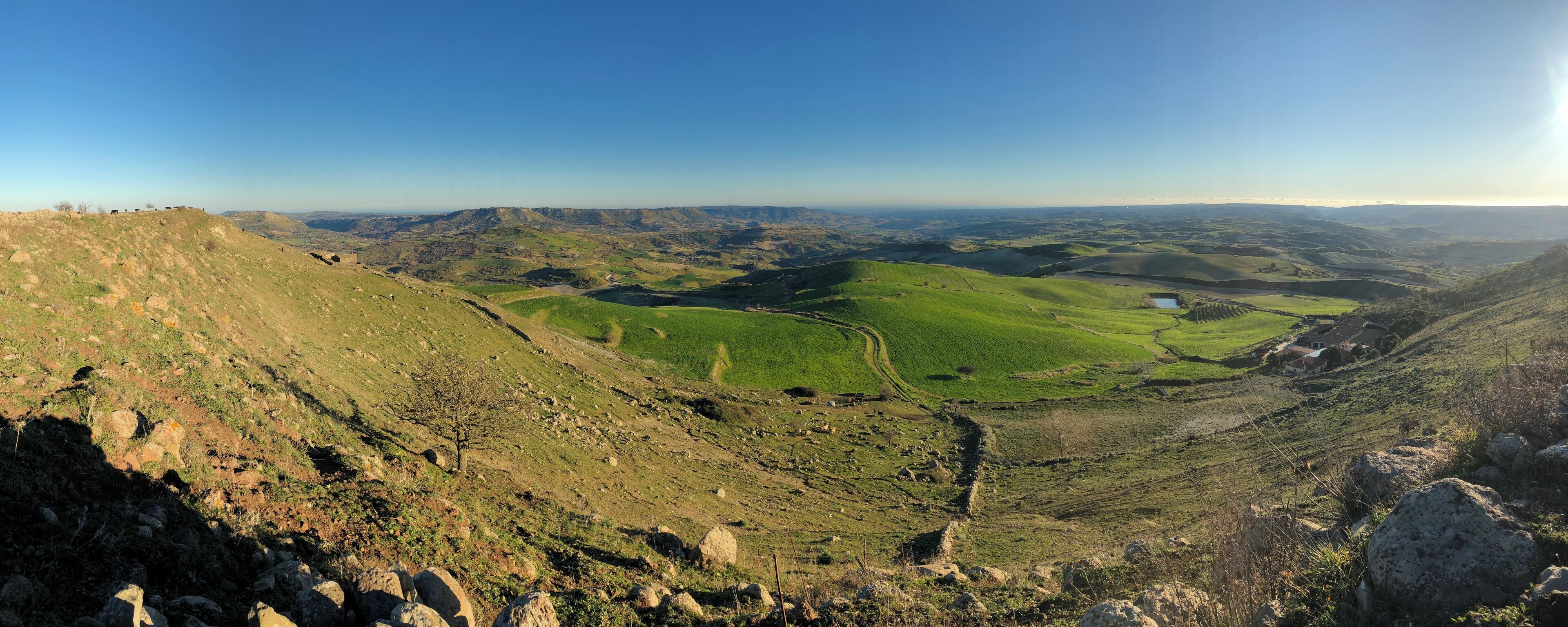 A valley with green fields, a small pond, and distant hills.