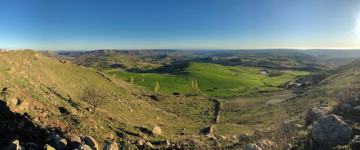 A valley with green fields, a small pond, and distant hills.