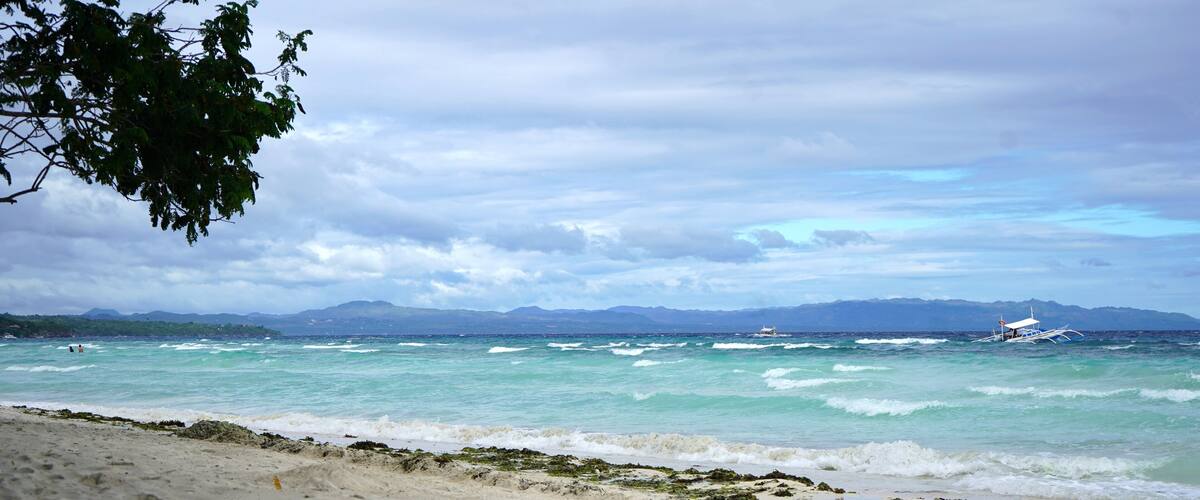 A beach with waves, a boat, and distant mountains.