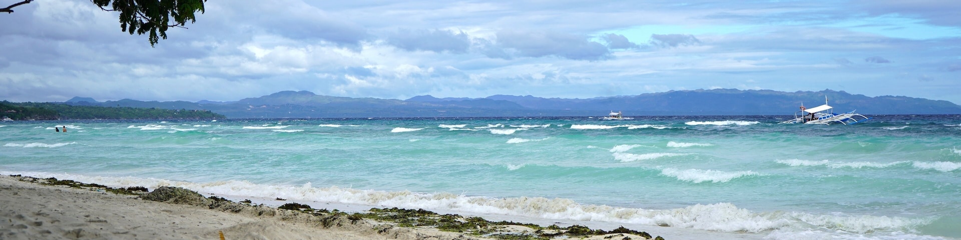 A beach with waves, a boat, and distant mountains.