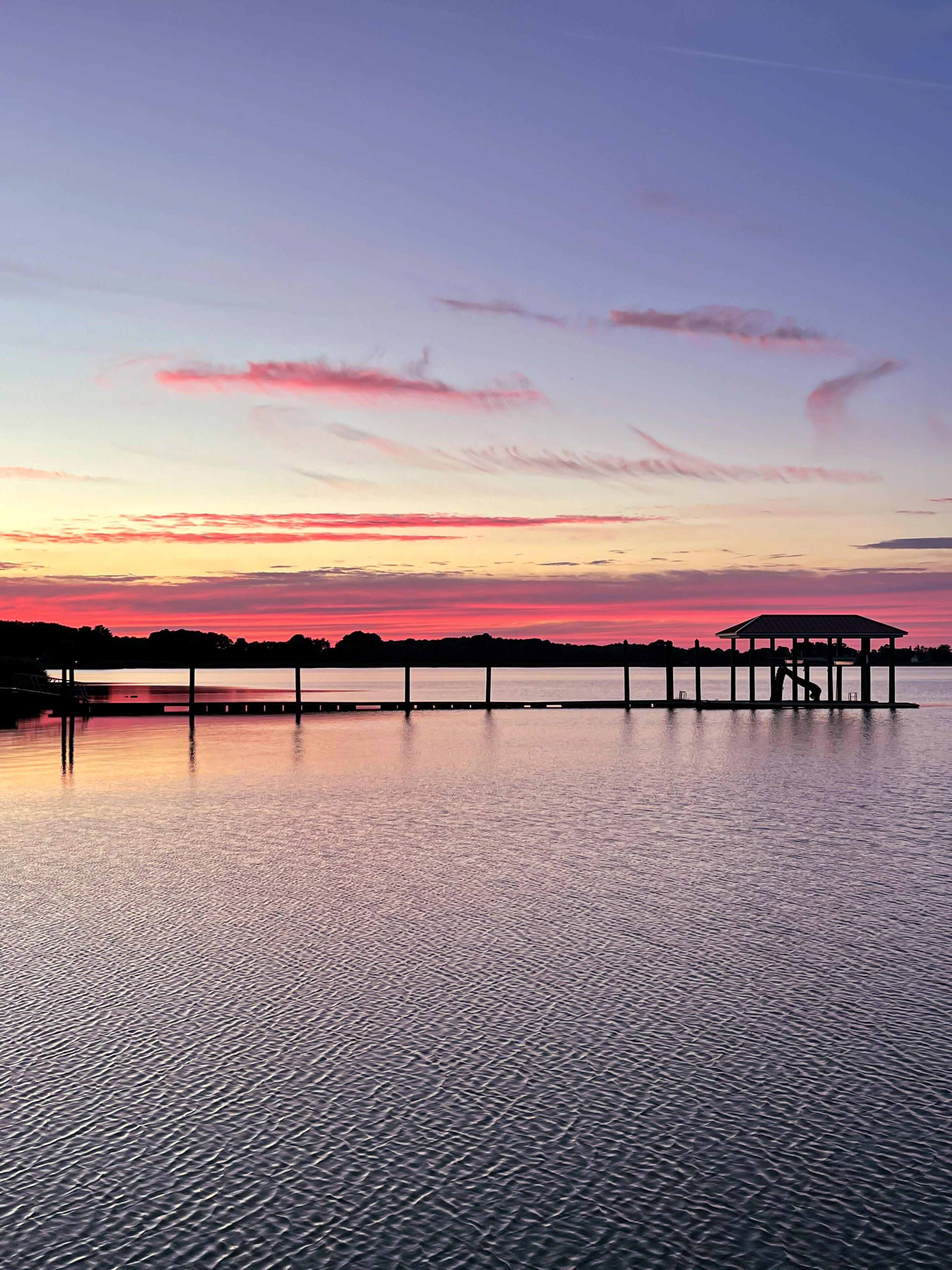 Ein Sonnenuntergang über einem ruhigen See mit einem Steg, der sich ins Wasser erstreckt.