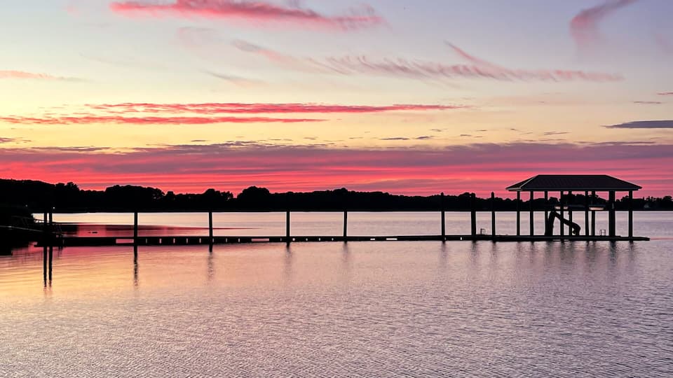 A sunset over a calm lake with a pier extending into the water.