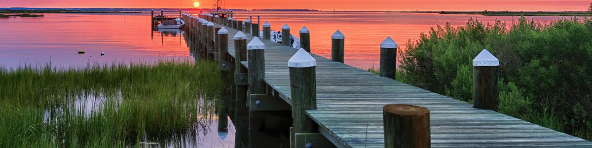 A wooden pier extending into a calm body of water, with a sunset in the background.