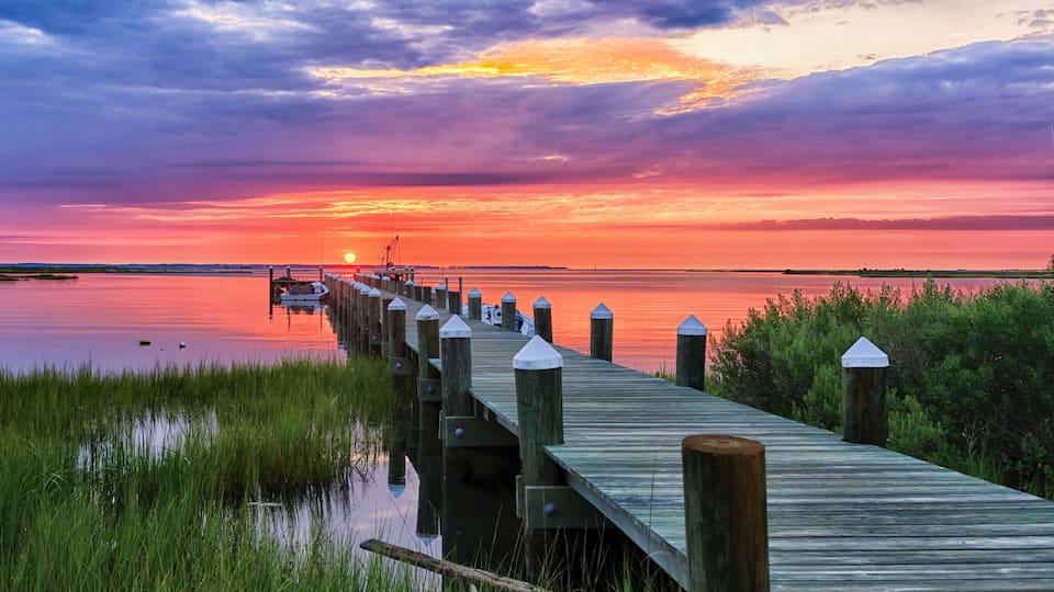 A wooden pier extending into a calm body of water, with a sunset in the background.