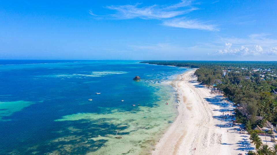 A coastal beach with clear turquoise waters, a sandy shore, and a pier extending into the sea.