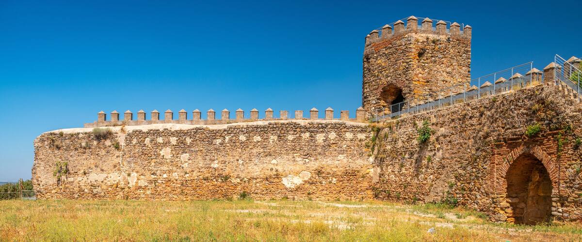 A historic stone wall with a watchtower and a large arched entrance.