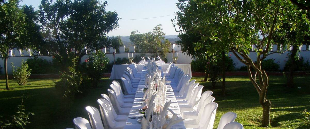 A long outdoor dining table set with white chairs and a floral centerpiece.