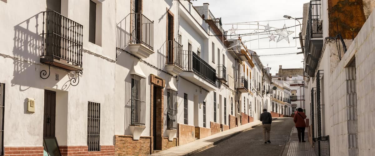 A narrow cobblestone street lined with white buildings with red brick bases and black iron balconies.