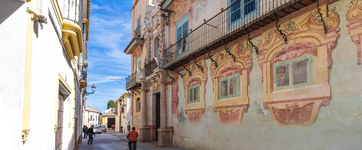 A narrow street with ornate buildings, a balcony, and a clear blue sky.