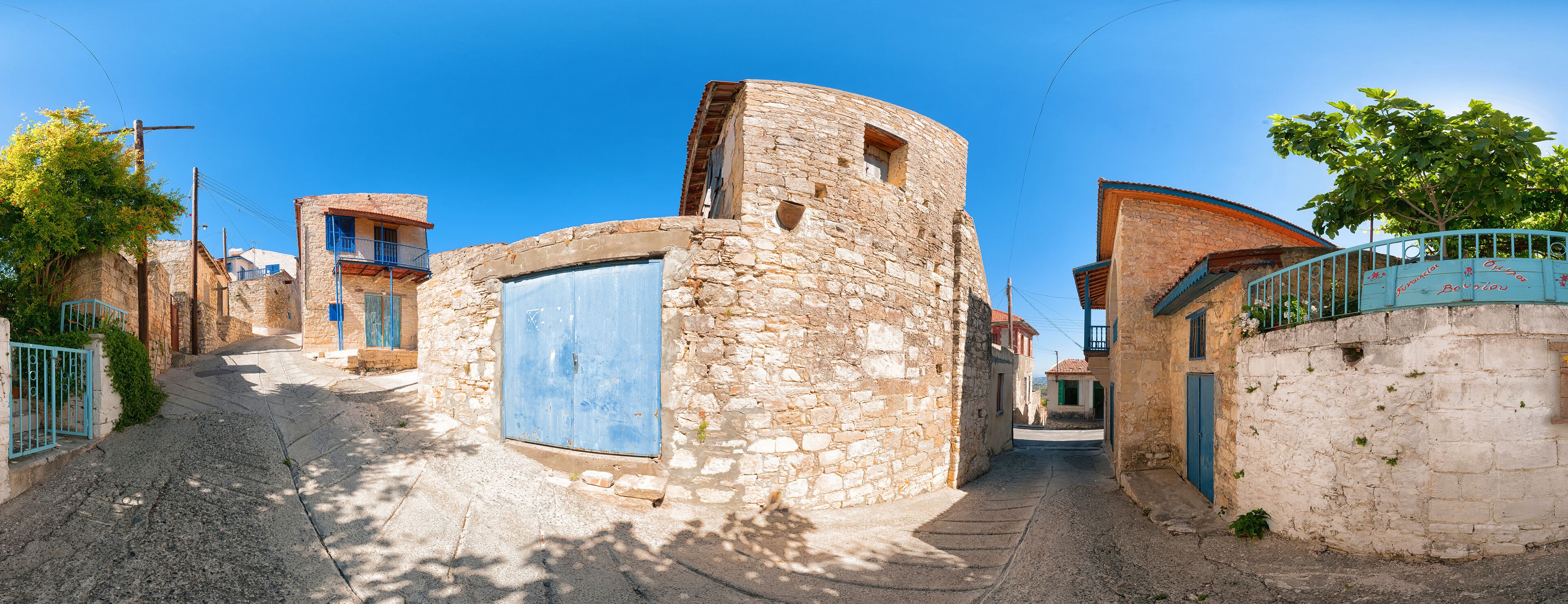 A narrow cobblestone street flanked by stone buildings with blue doors and balconies.