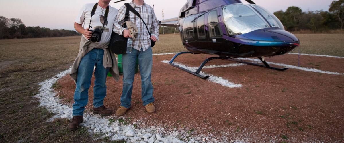 Two people standing on a gravel path with a helicopter in the background.
