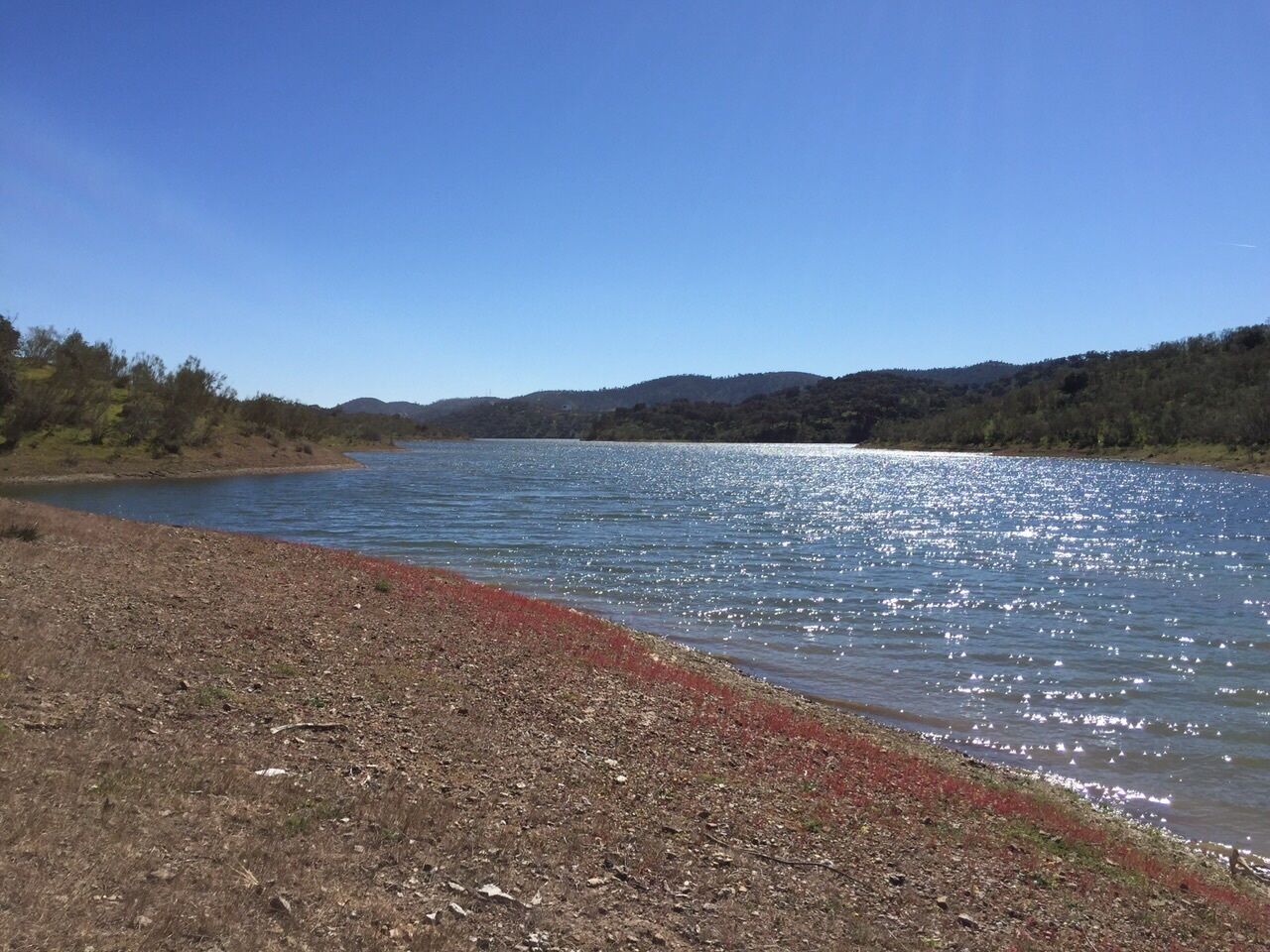 A calm lake with a rocky shoreline and distant hills.