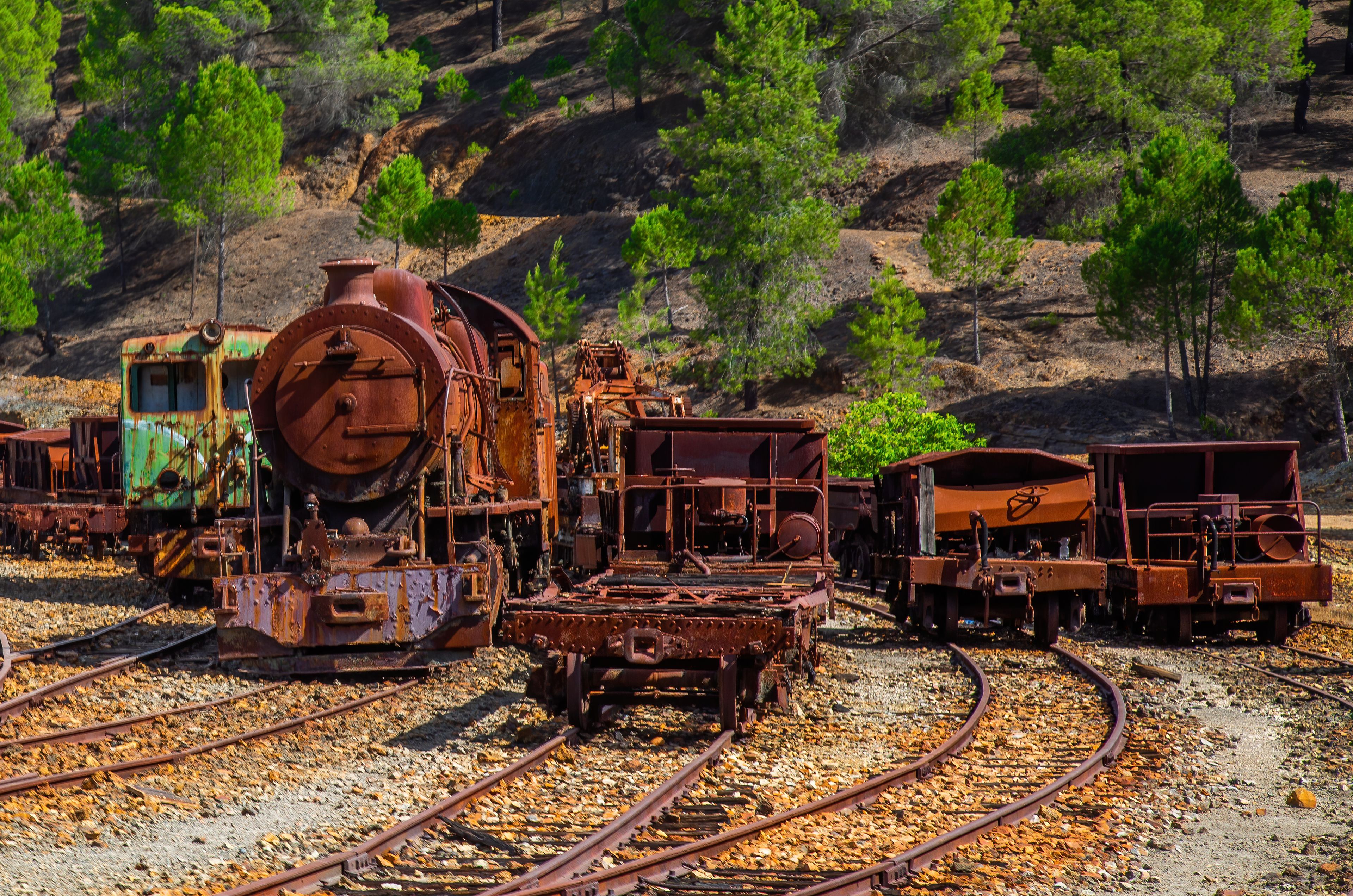 Eine Sammlung verrosteter, verlassener Eisenbahngleise und Lokomotiven in einer trockenen, hügeligen Landschaft mit spärlicher Vegetation.