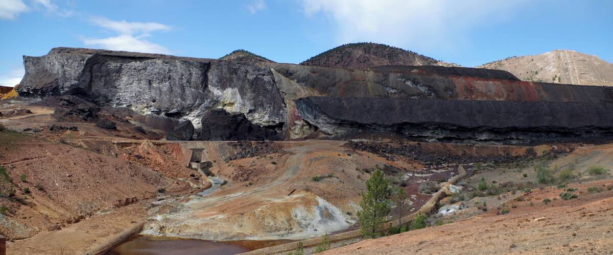A large open-pit mine with exposed rock layers and a small pond.