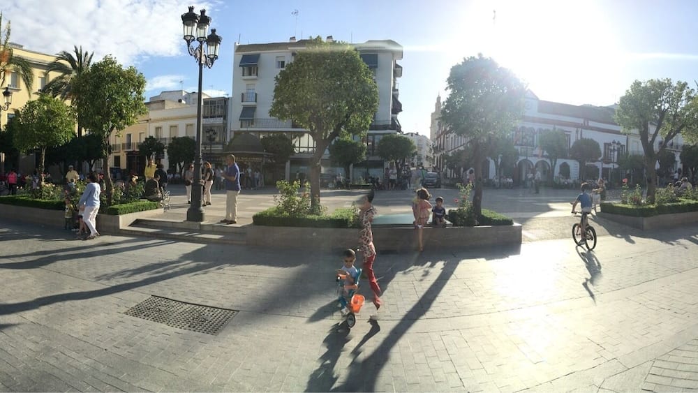 Ein sonniger Platz mit Menschen, Bäumen und historischen Gebäuden.