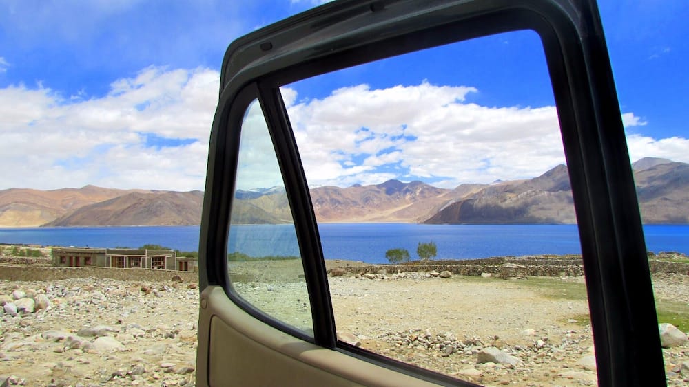A car's side window with a view of a lake, mountains, and a clear sky.